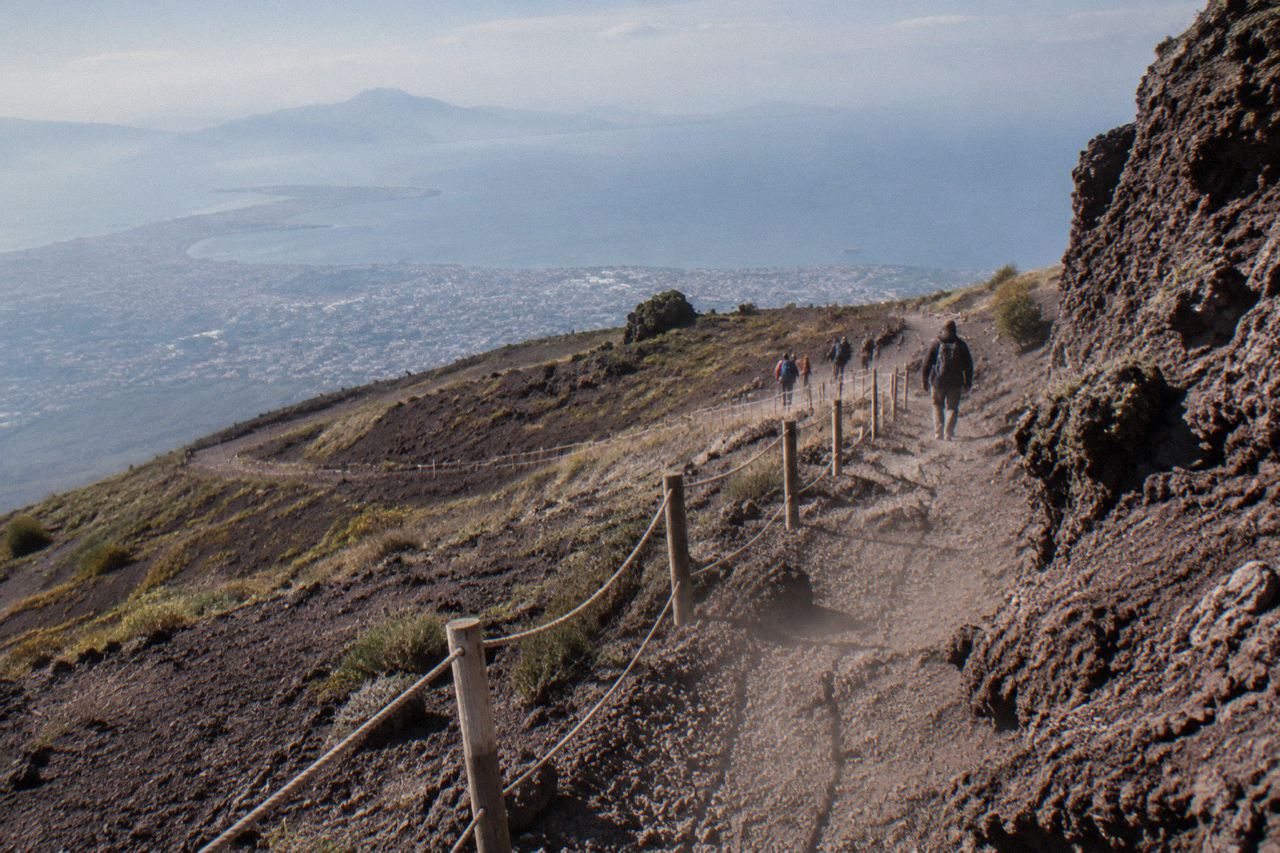 Hikers on the switchback gravel trail of the Gran Cono climbing toward the crater rim of Vesuvius, seen from behind